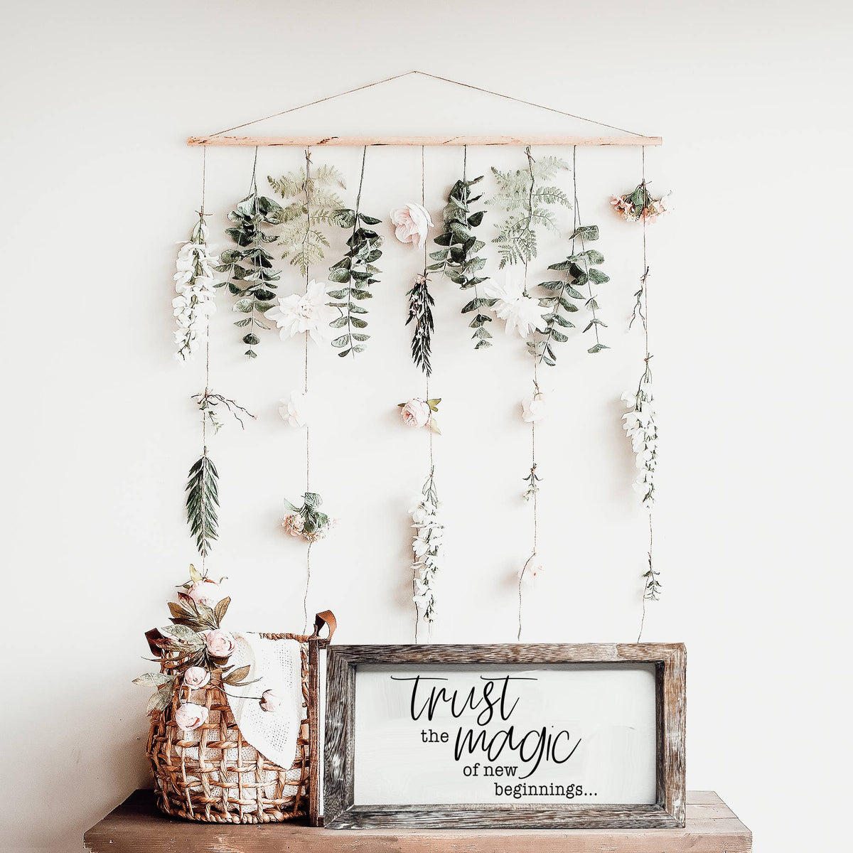 Trust Magic wooden sign on a shelf beneath hanging flowers and greenery.